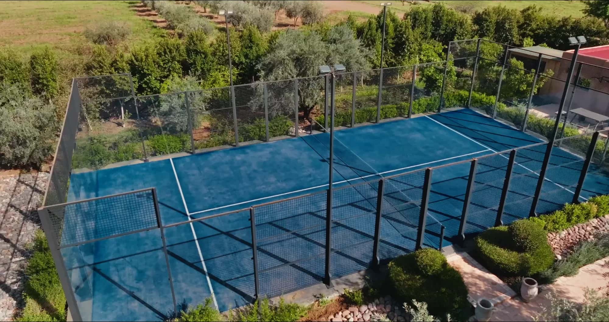 Aerial drone view of the private padel court at Villa Yemna in Marrakech, surrounded by fencing and the estate olive grove.