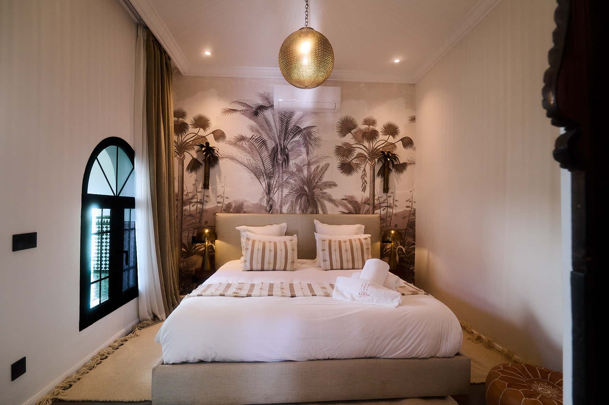 Suite Ben Haddou bedroom at Villa Yemna, with embroidered white bedding, a Moroccan pendant light, and a botanical wall mural.