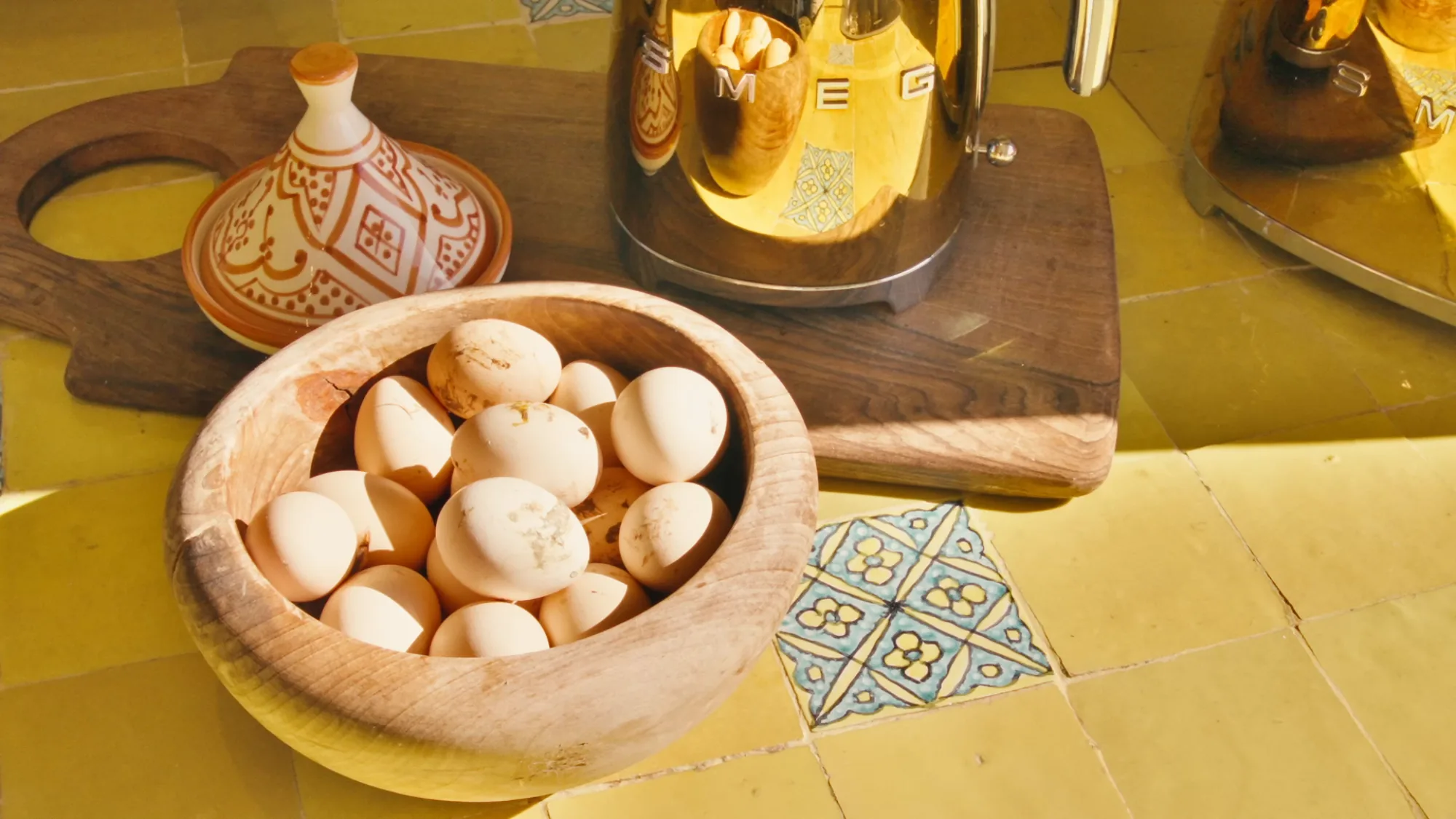 Détail dans la cuisine du riad de Villa Yemna avec bol d'œufs frais en bois, bouilloire SMEG dorée et plan de travail en zellige jaune.
