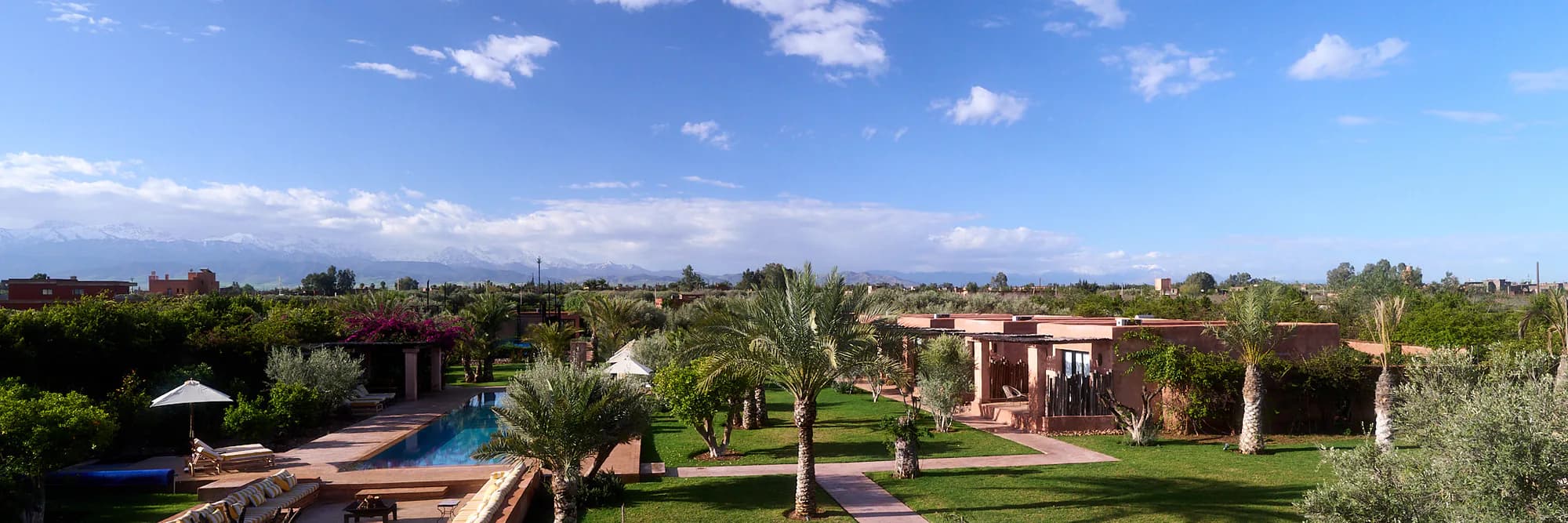 Vue panoramique sur le domaine de Villa Yemna avec piscine, jardins, palmiers, suites bungalow et montagnes de l'Atlas.