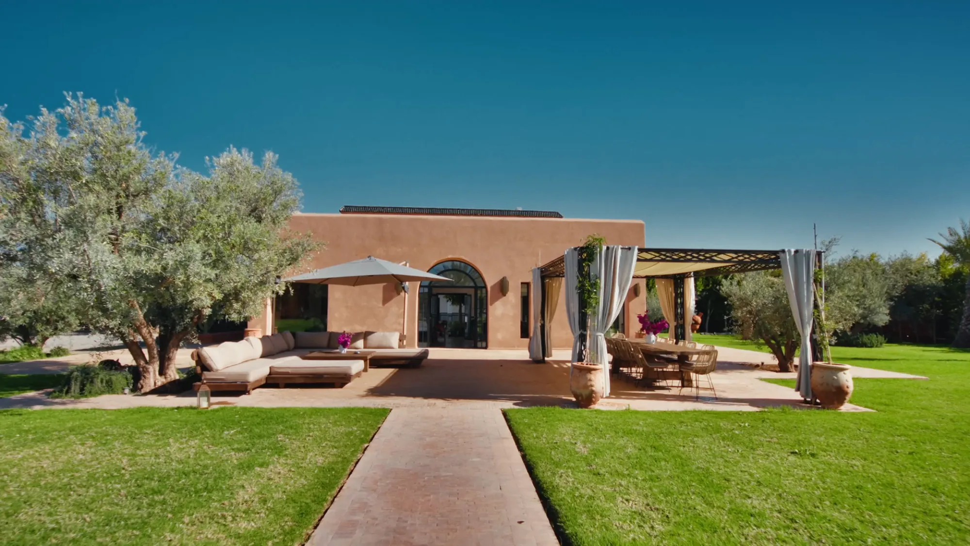 Façade of a Villa Yemna building in Marrakech with bamboo pergola, white curtains, outdoor lounge and fuchsia bougainvillea.