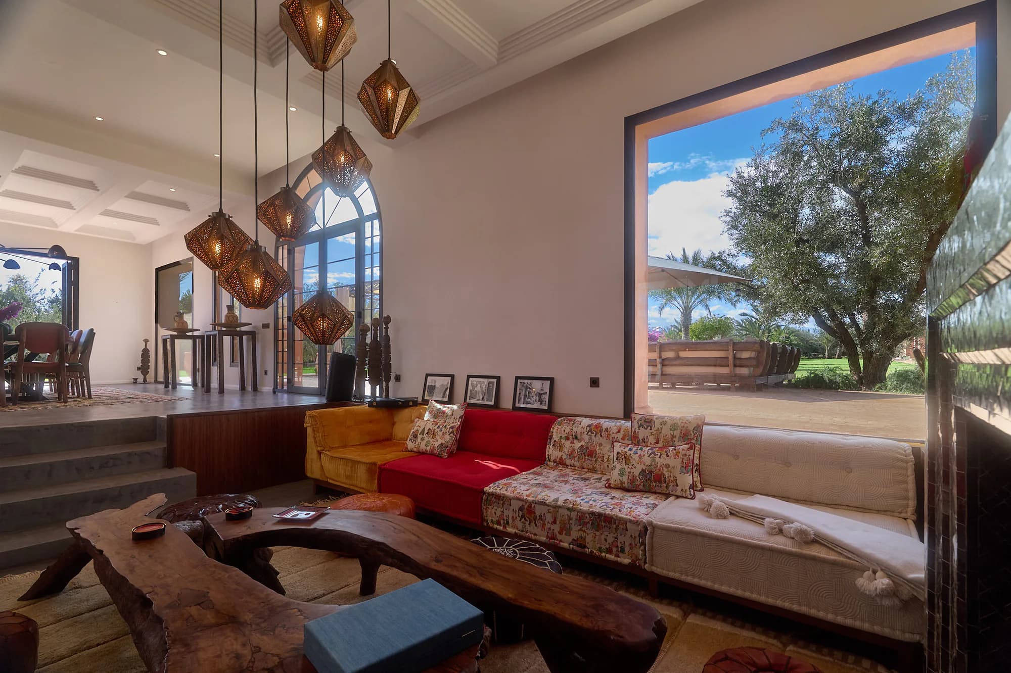 Salon du riad de Villa Yemna avec canapés à motifs, lanternes suspendues, cheminée en zellige et grande fenêtre ouverte sur le jardin.