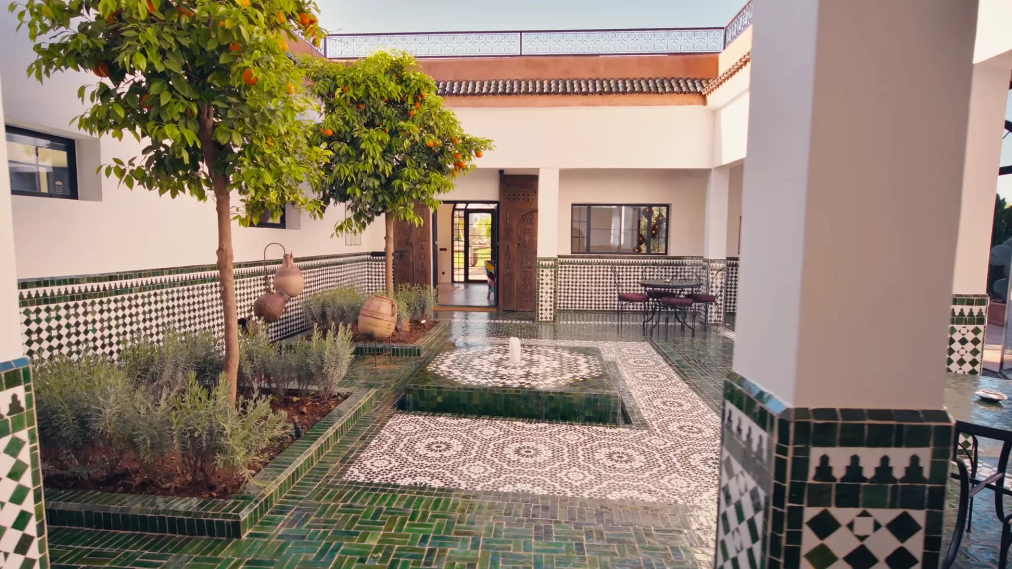 Cour intérieure du riad de Villa Yemna à Marrakech avec fontaine centrale, sol en zellige vert brillant, oranger et arcades traditionnelles marocaines.