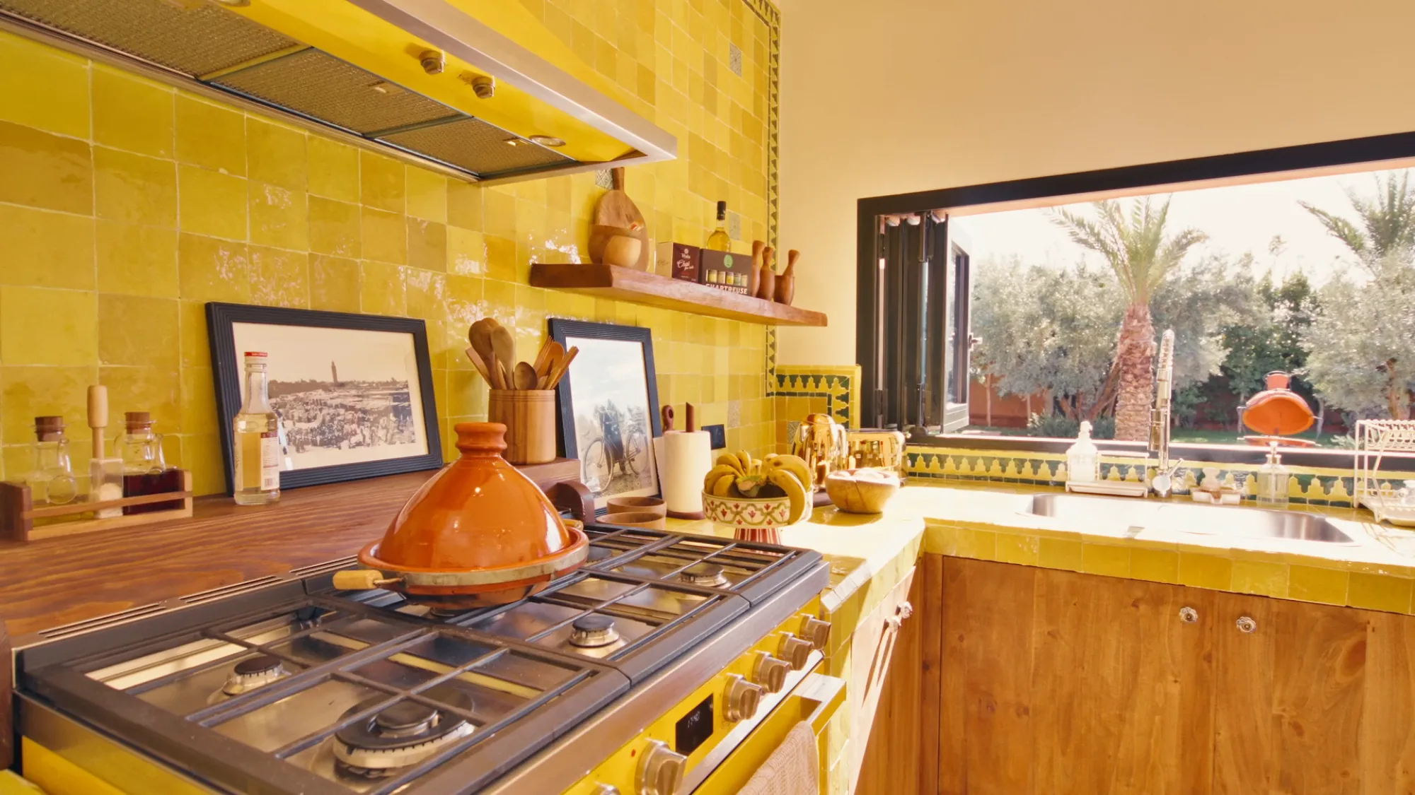 Cuisine du riad de Villa Yemna à Marrakech avec tagine traditionnel orange posé sur la cuisinière, étagères et zelliges jaunes.