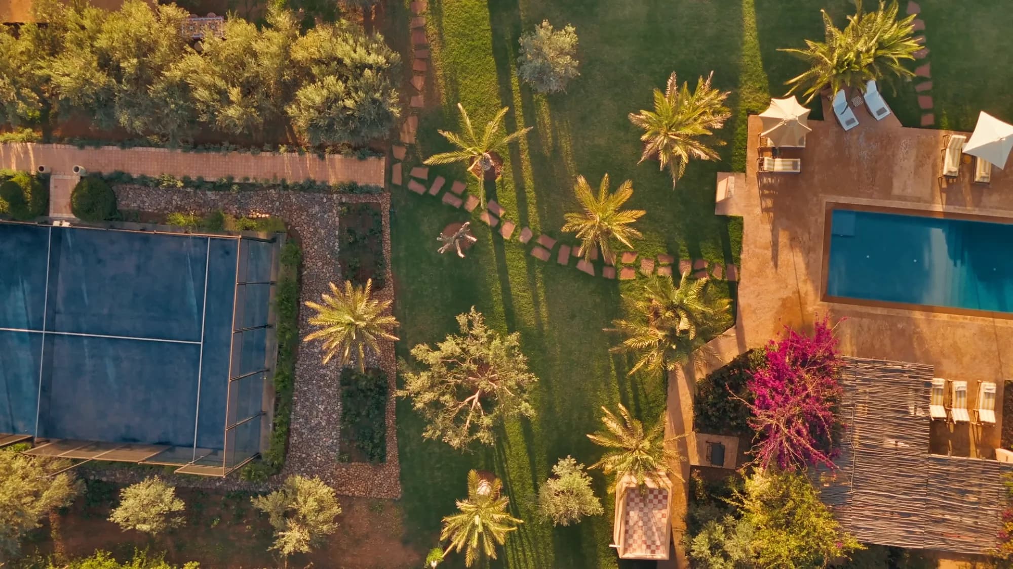 Golden hour aerial view of Villa Yemna in Marrakech with blue padel court, pool and date palm garden.