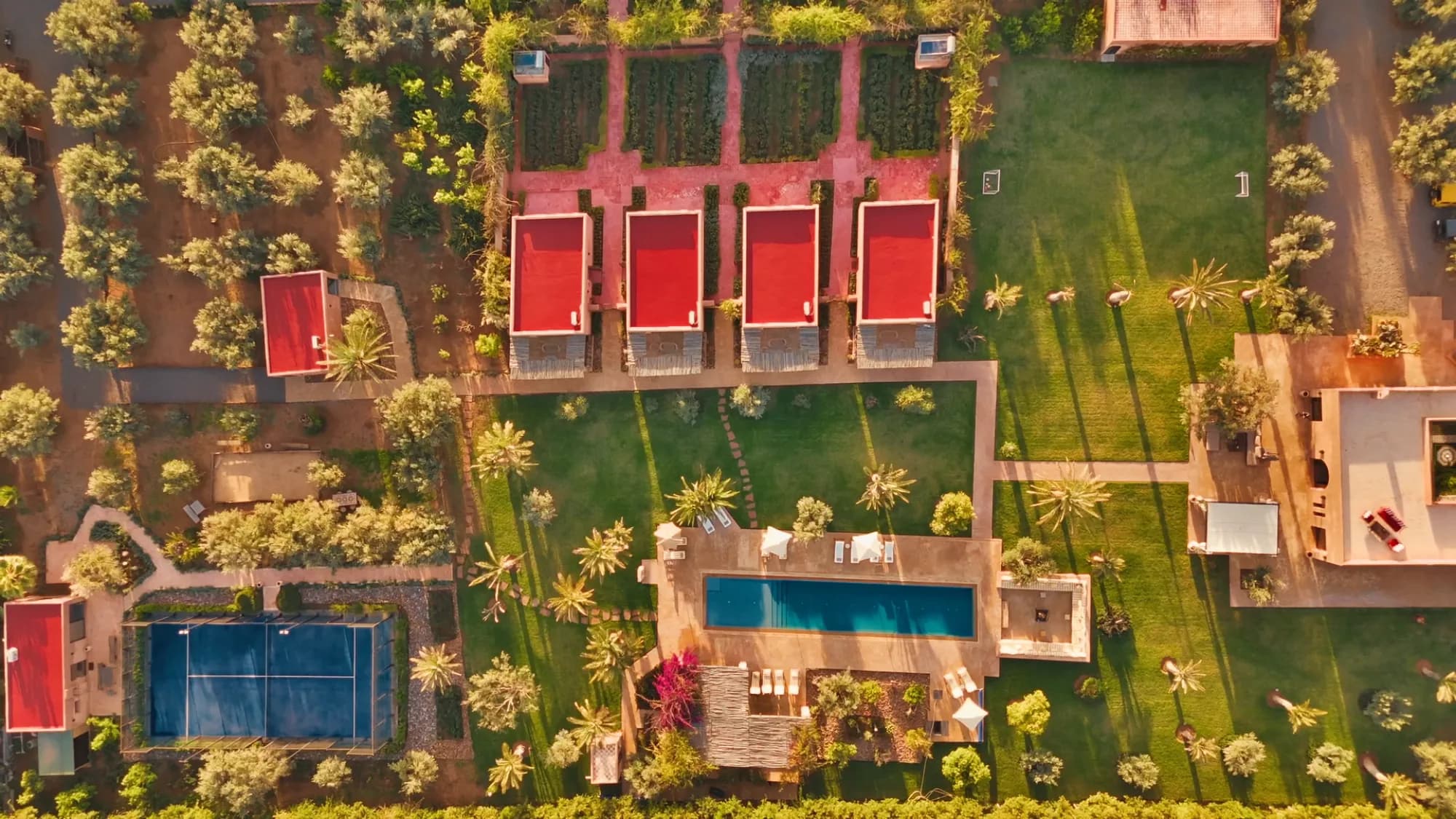 Vue drone du domaine entier de Villa Yemna à Marrakech avec les 4 suites bungalow à toits rouges, la piscine au sel, le terrain de padel et les jardins.