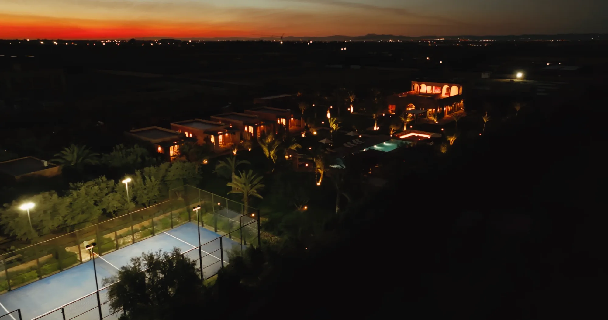 Vue drone nocturne du domaine de Villa Yemna et du terrain de padel au coucher du soleil.