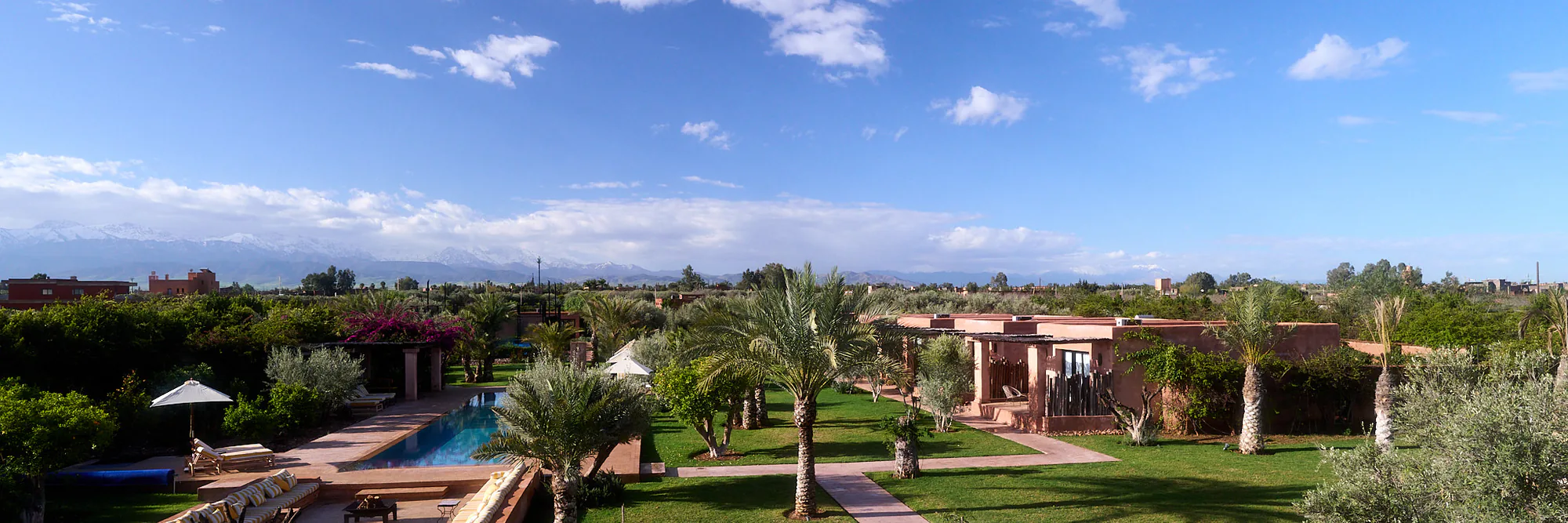 Vue panoramique sur le domaine de Villa Yemna avec piscine, jardins, palmiers, suites bungalow et montagnes de l'Atlas.