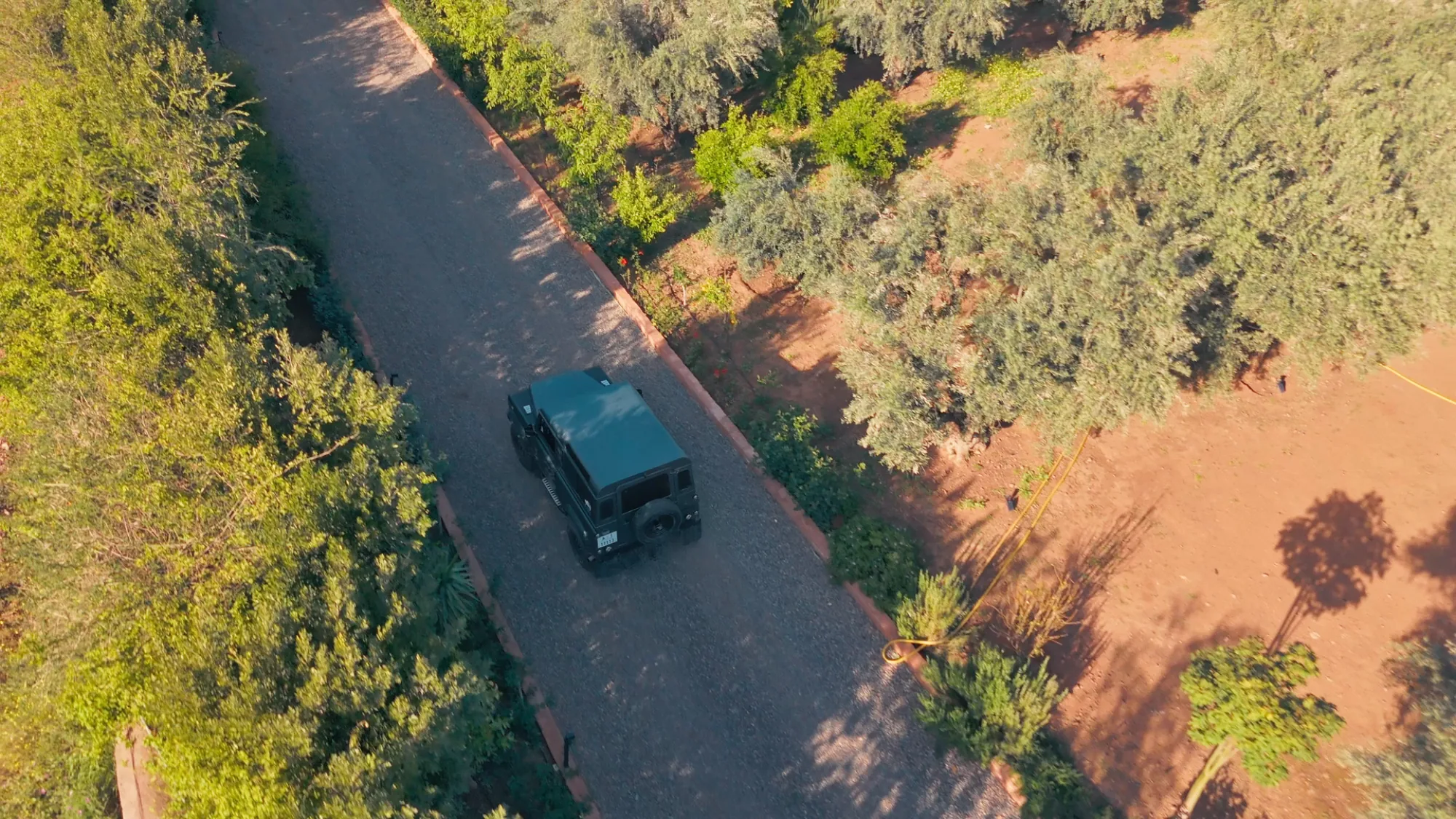 Vue aérienne d'un 4x4 noir arrivant à Villa Yemna à Marrakech sur l'allée bordée de haies vertes et d'oliviers.