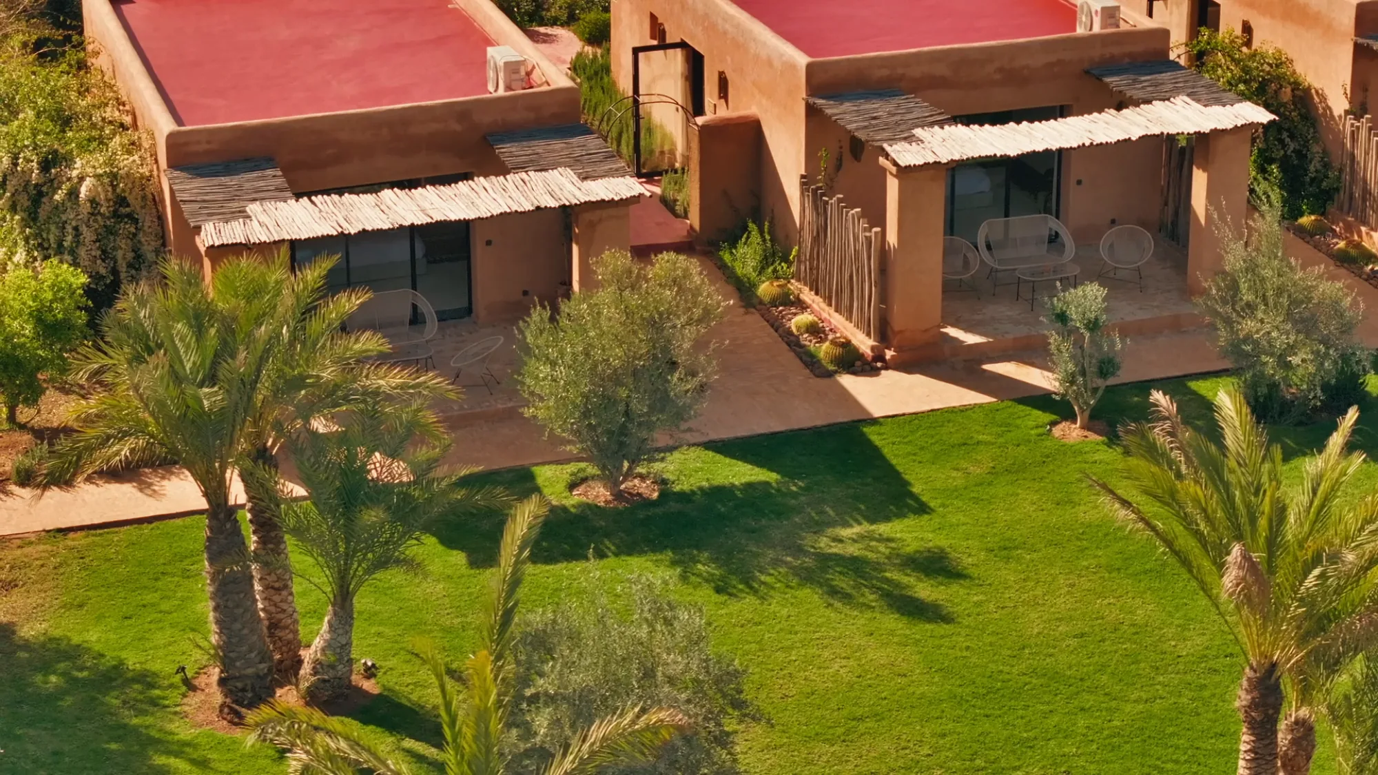Vue aérienne de deux suites bungalow de Villa Yemna à Marrakech avec toits rouges, pergolas en bambou, terrasses privées et jardin.