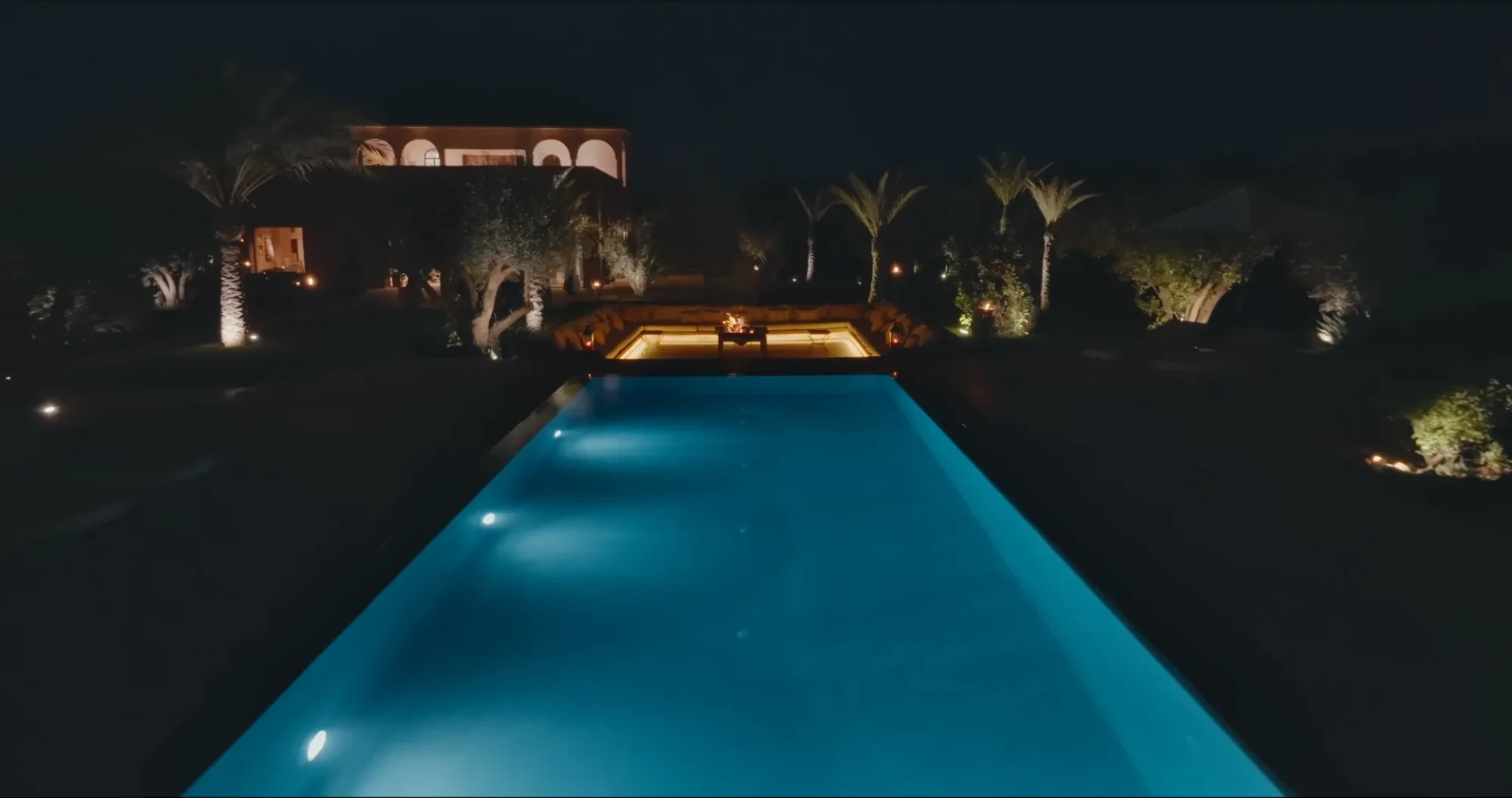 Piscine de Villa Yemna à Marrakech illuminée de nuit, avec riad éclairé en arrière-plan et palmiers.