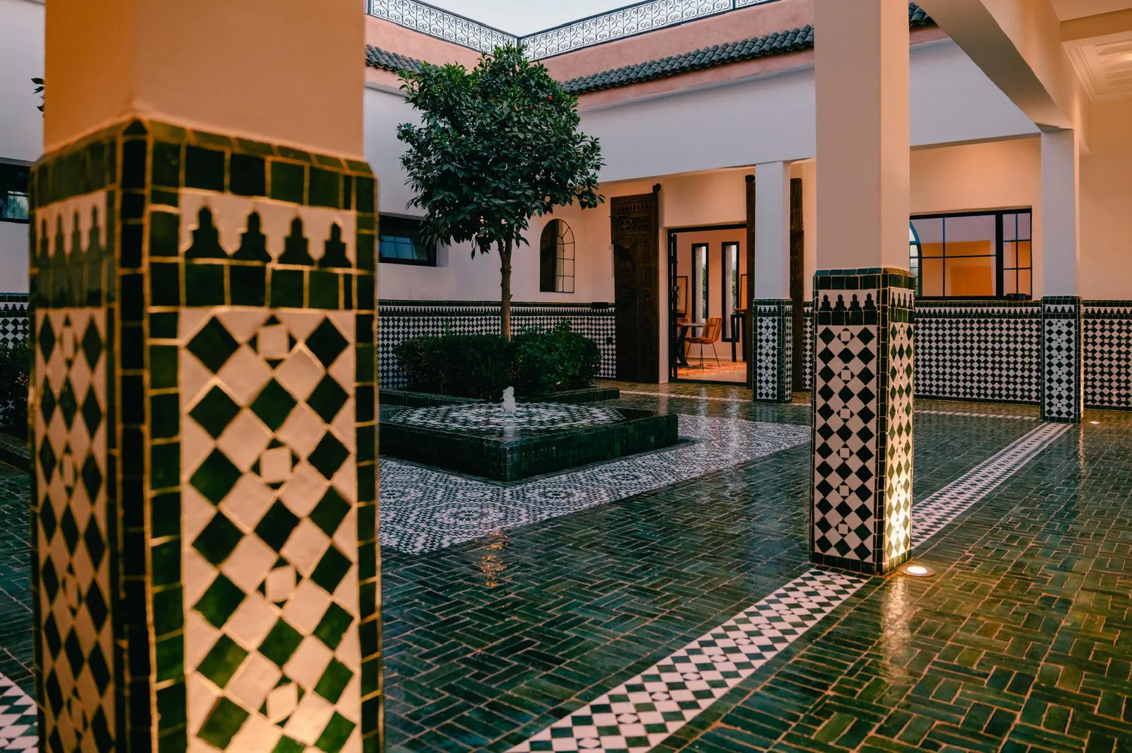 Cour intérieure du riad de Villa Yemna au crépuscule, avec sol en zellige vert brillant, colonnes décorées et lumières chaudes.