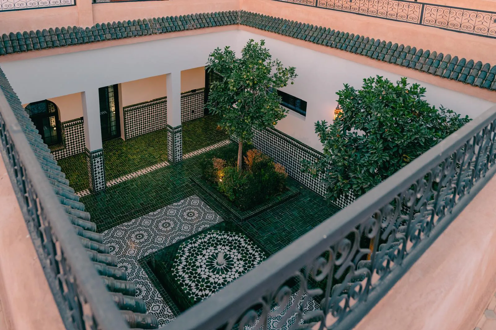 Cour intérieure du riad de Villa Yemna à Marrakech vue depuis l'étage, avec zelliges verts, orangers, fontaine centrale et arcades marocaines.