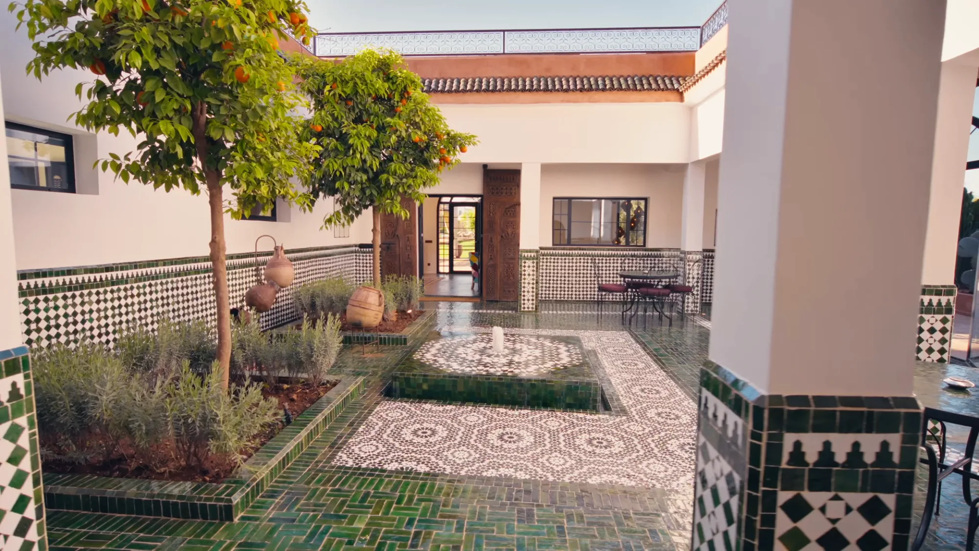 Cour intérieure du riad de Villa Yemna à Marrakech avec fontaine centrale, sol en zellige vert brillant, oranger et arcades traditionnelles marocaines.