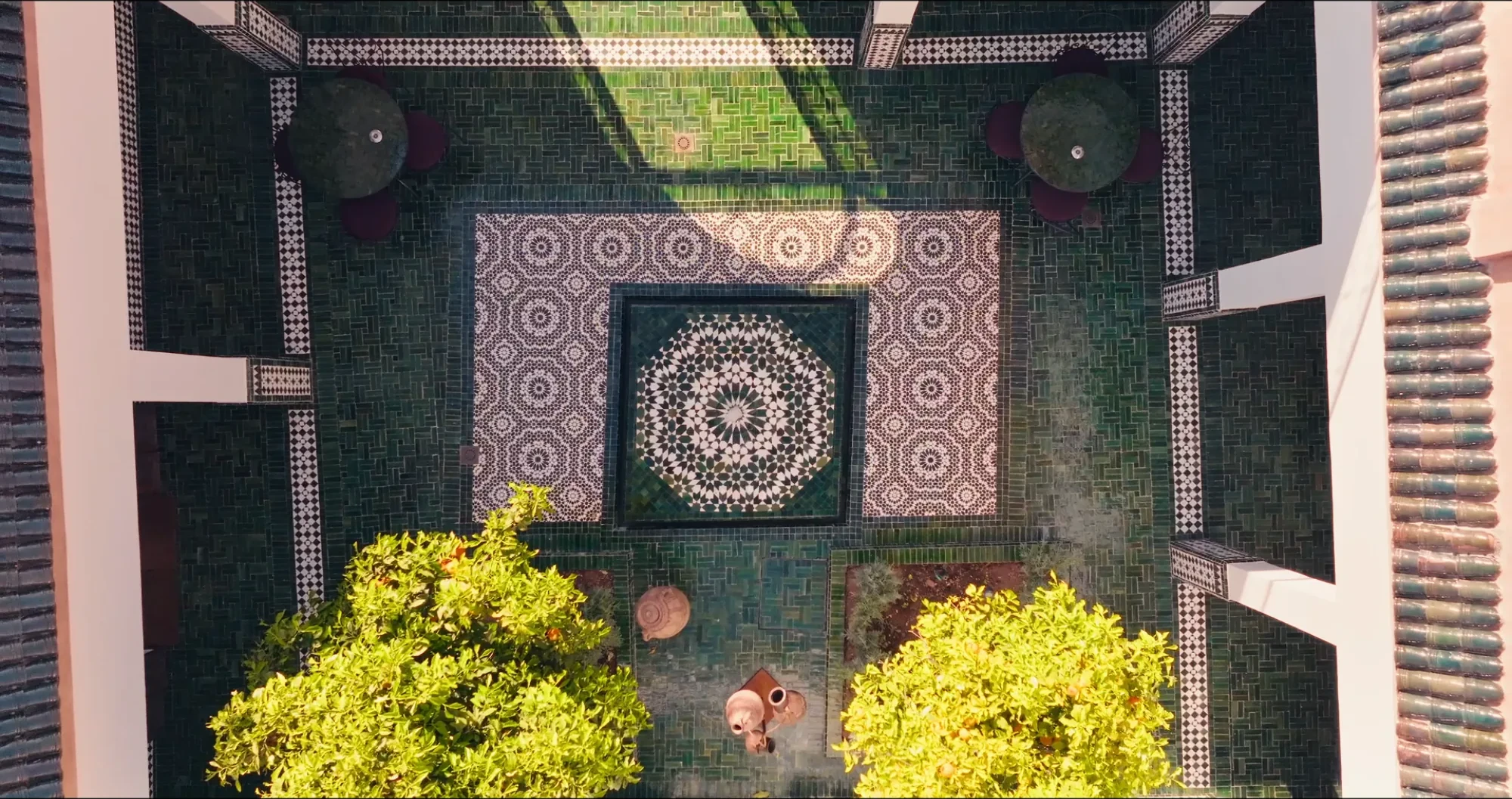 Vue plongeante de la cour intérieure du riad de Villa Yemna à Marrakech, avec sol en zellige orné de rosaces marocaines et orangers en pot.