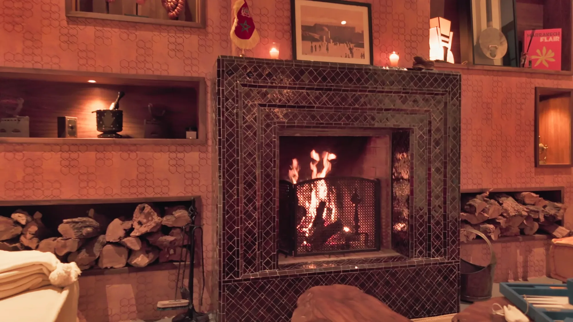 Cheminée habillée de zelliges noirs avec feu crépitant et bûches empilées, dans le salon du riad de Villa Yemna à Marrakech.