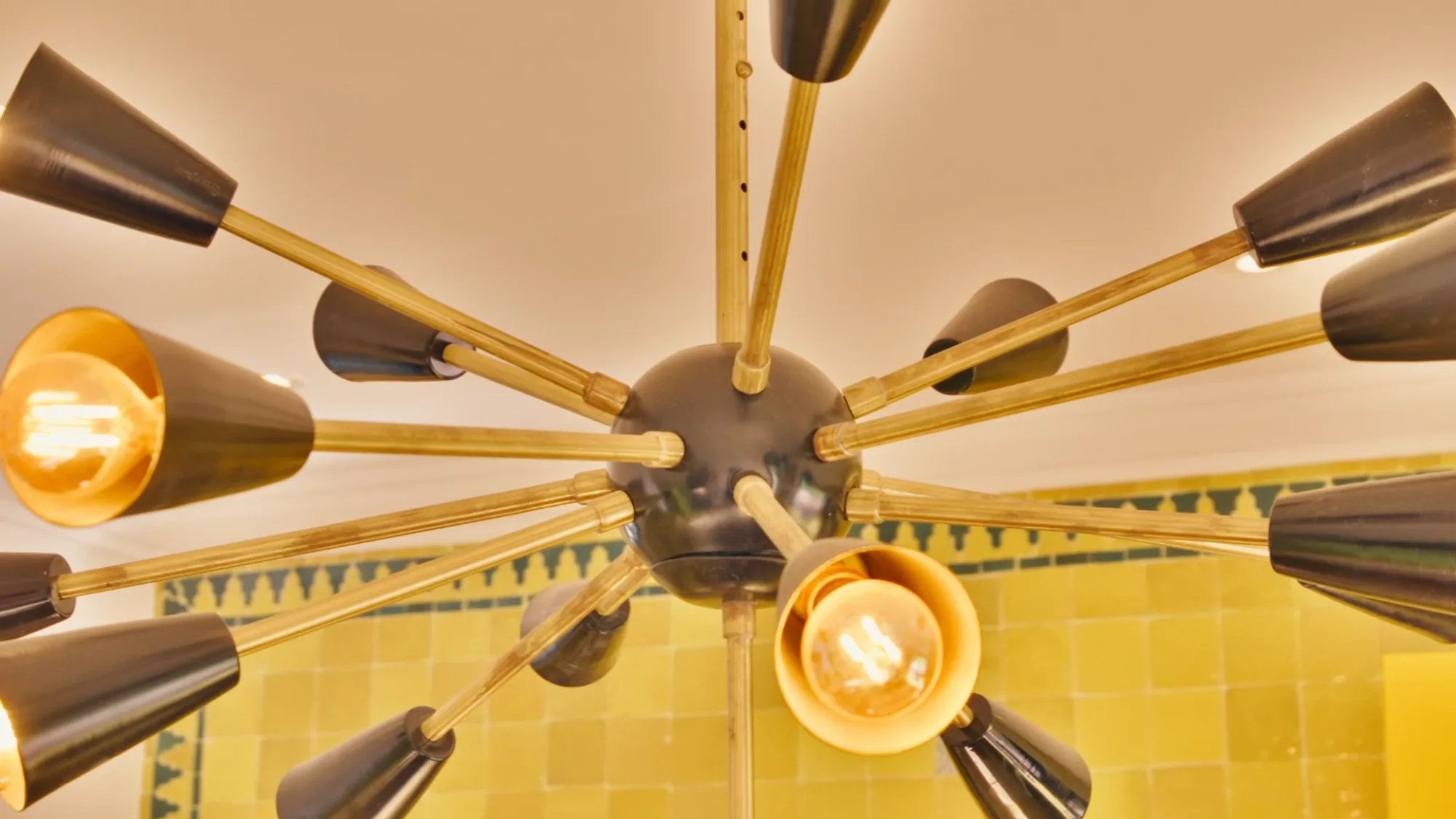 Gros plan sur le lustre sputnik moderne de la cuisine du riad de Villa Yemna à Marrakech, sur fond de zelliges jaunes.