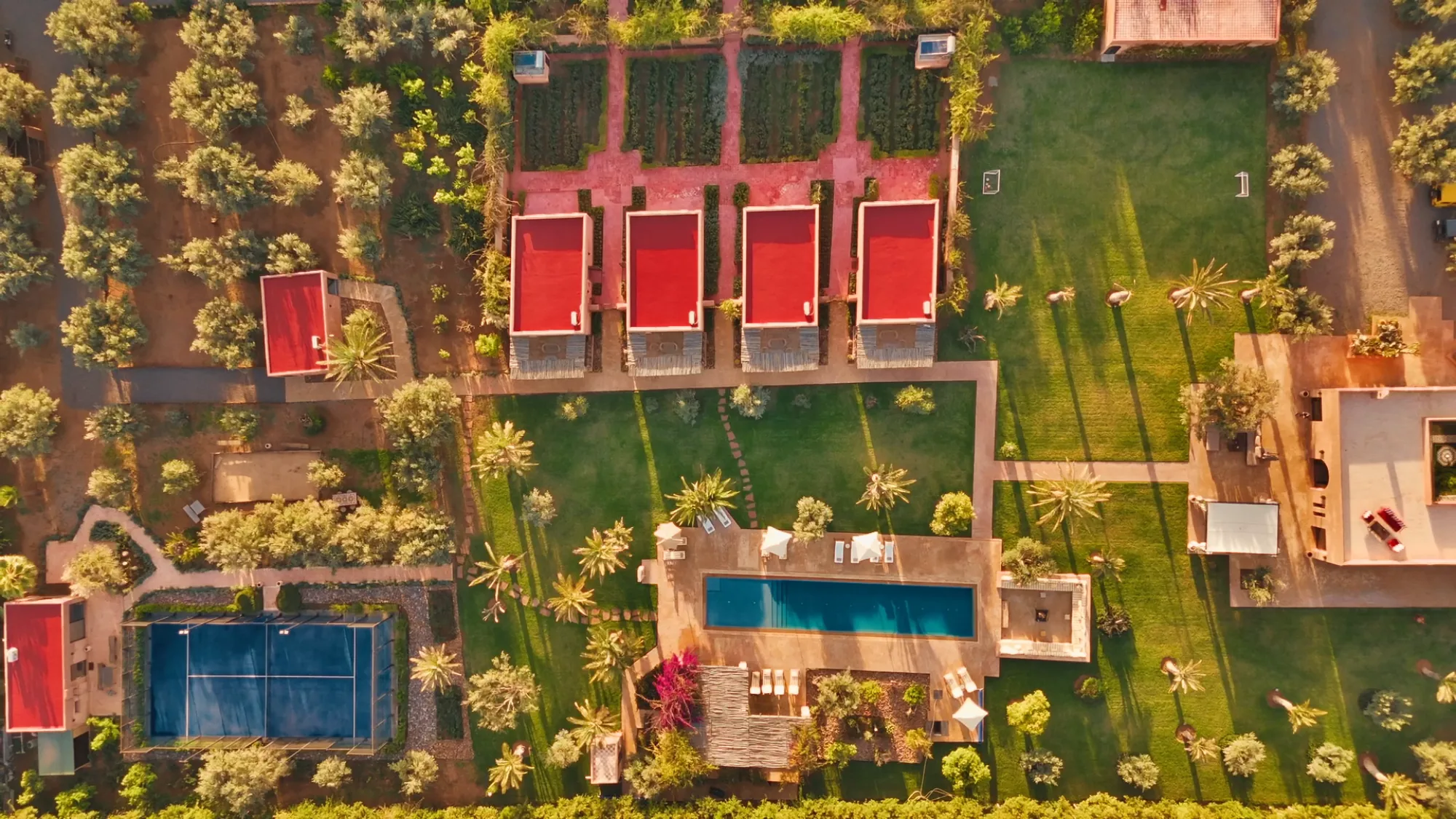 Vue drone du domaine entier de Villa Yemna à Marrakech avec les 4 suites bungalow à toits rouges, la piscine au sel, le terrain de padel et les jardins.