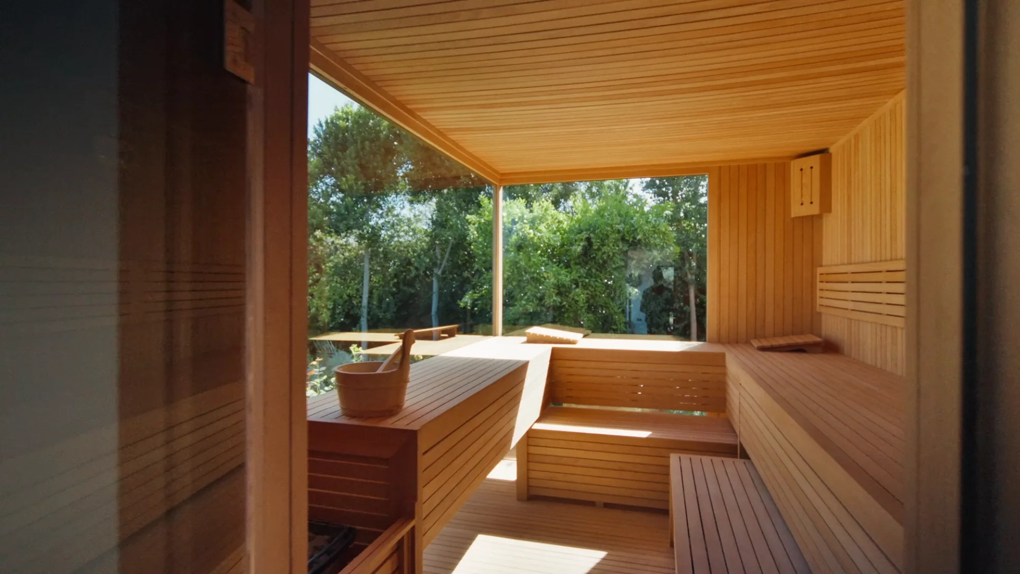 Sauna privé de Villa Yemna à Marrakech en bois clair avec bancs, plafond lambrissé et grande baie vitrée ouvrant sur le jardin.