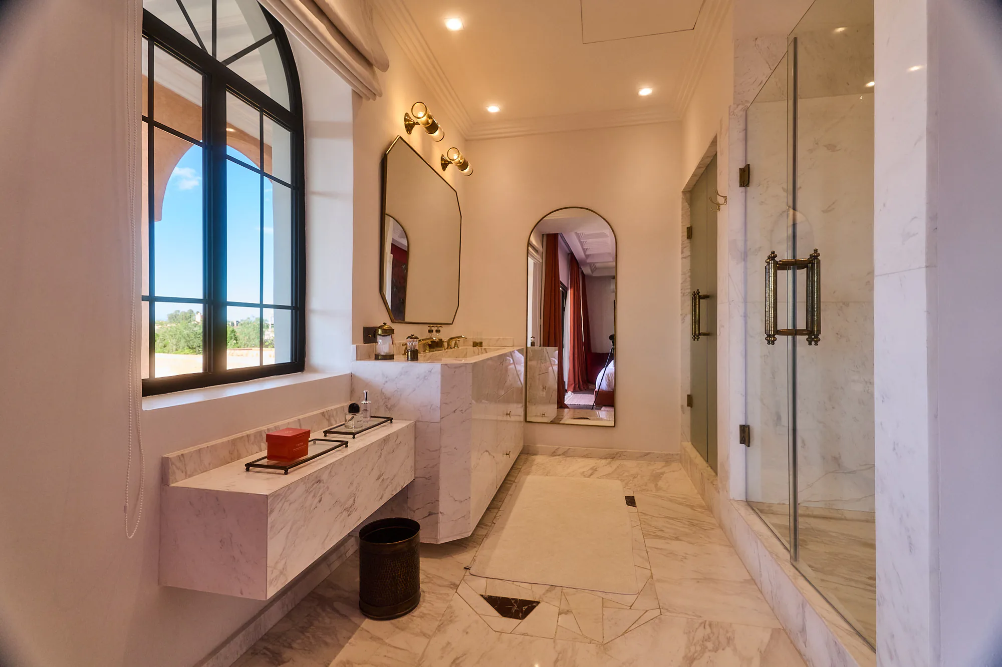 Grande salle de bain en marbre de Villa Yemna avec double vasque, robinetterie en laiton, douche vitrée et miroir pleine hauteur.
