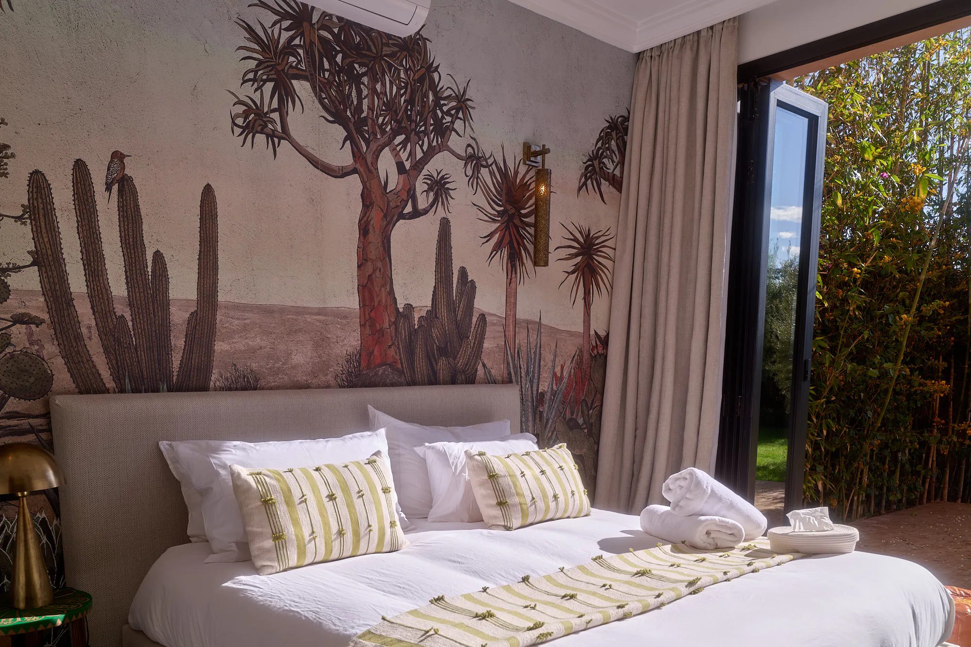 Chambre de suite à Villa Yemna avec fresque de cactus, lit blanc lumineux, coussins brodés et ouverture sur la terrasse privée.
