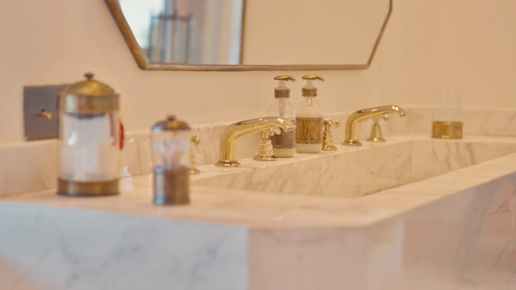 Salle de bain d'une suite de Villa Yemna à Marrakech avec double vasque en marbre, robinetterie en laiton et miroir arqué.