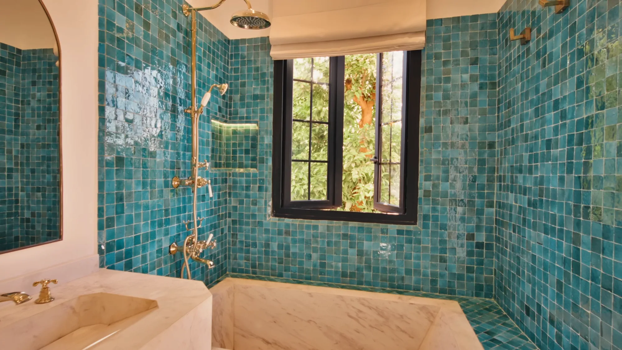 Salle de bain de la Chambre Taghazout à Villa Yemna à Marrakech, avec zelliges bleu-vert, baignoire en marbre, douche laiton et fenêtre sur la végétation.