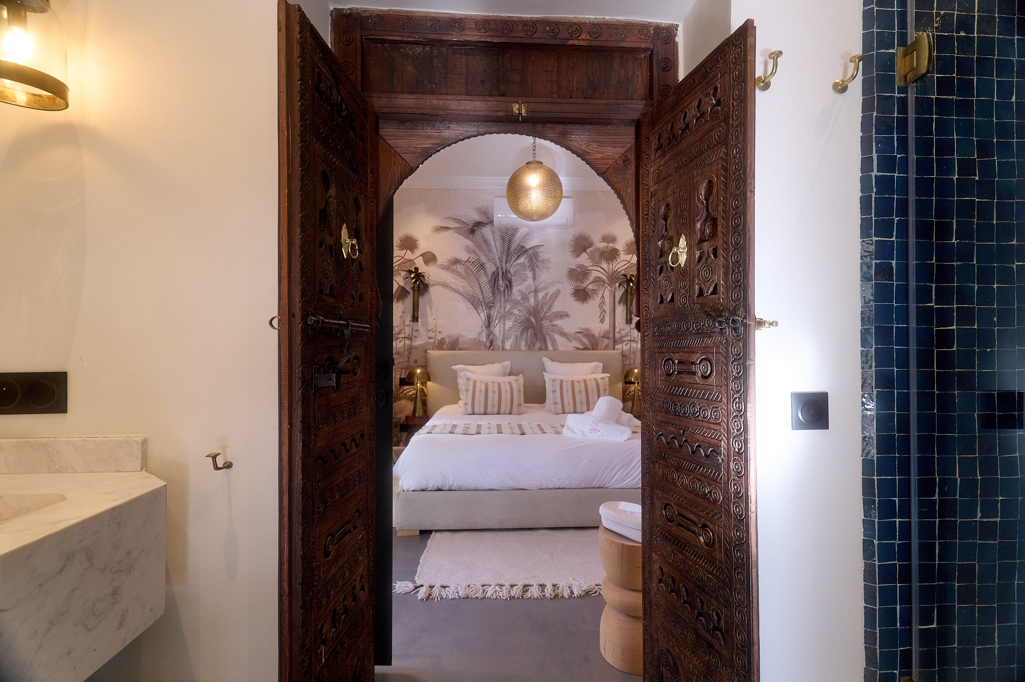 Vue de la chambre de la Suite Ben Haddou depuis la salle de bain partagée, encadrée par des portes marocaines sculptées.